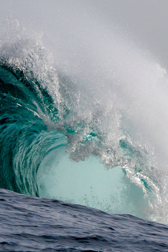 Powerful wave crashing in the ocean with a gray sky.
