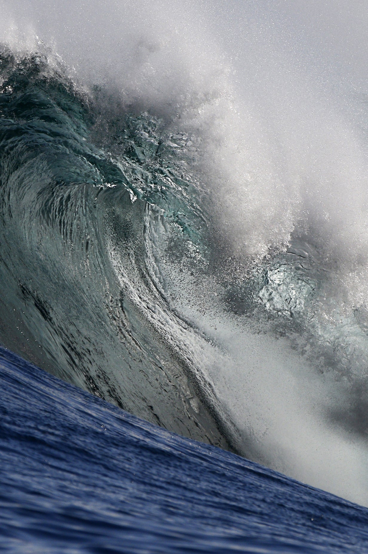 Towering wave with white foam against a gray sky